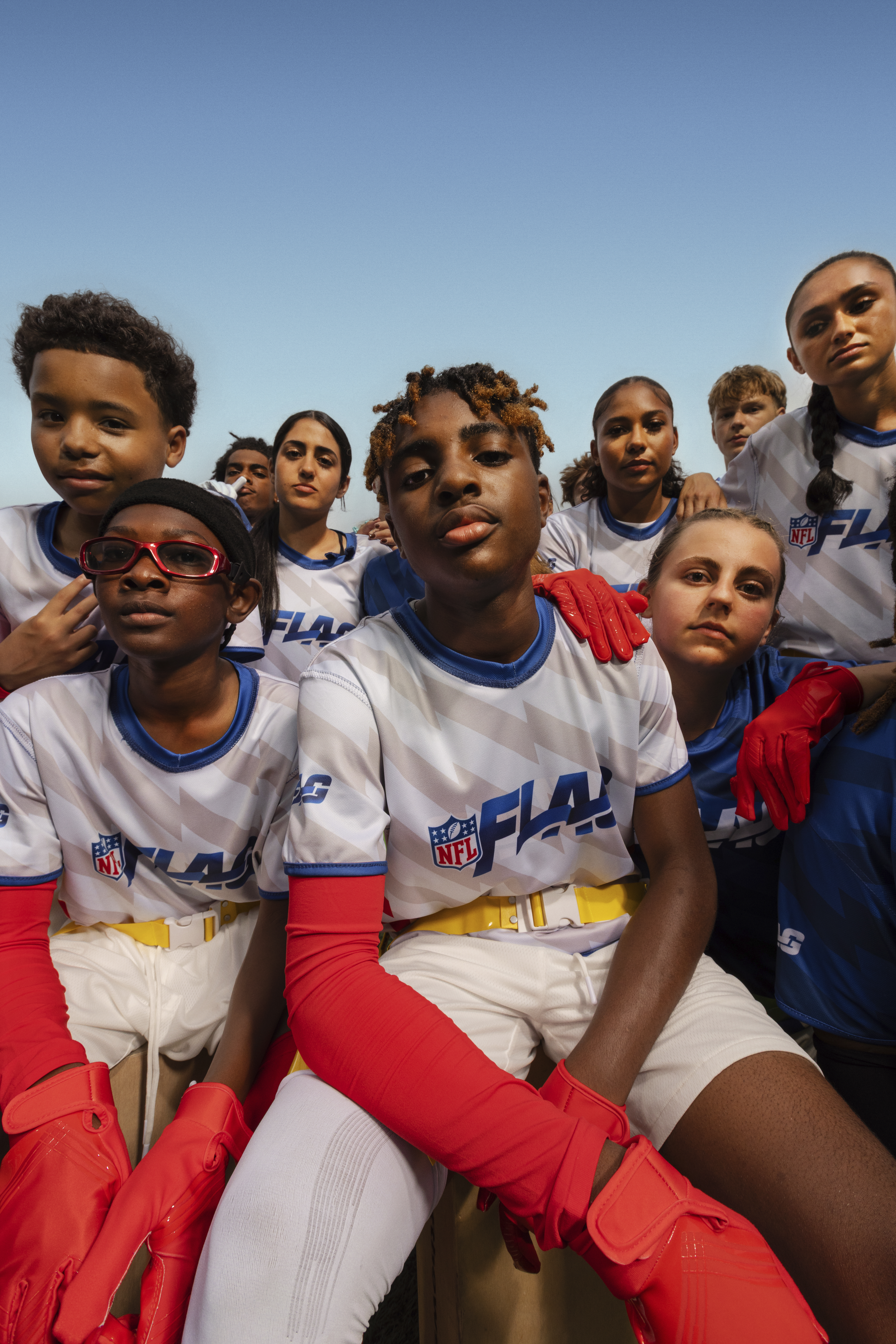 A diverse group of young players in NFL Flag uniforms posing together outdoors.